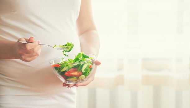 A pregnant woman eats a salad with vegetables. Selective focus. Food.