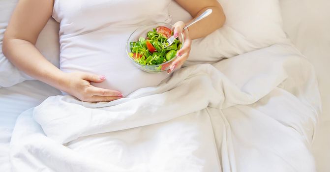 A pregnant woman eats a salad with vegetables. Selective focus. Food.