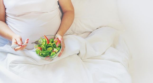 A pregnant woman eats a salad with vegetables. Selective focus. Food.