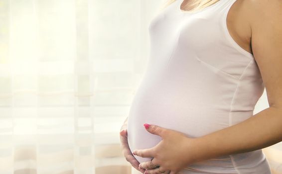 A pregnant woman hugs her belly. Selective focus. People.