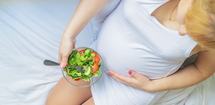 A pregnant woman eats a salad with vegetables. Selective focus. Food.