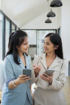 Two female business colleagues standing in office and using smart phone.