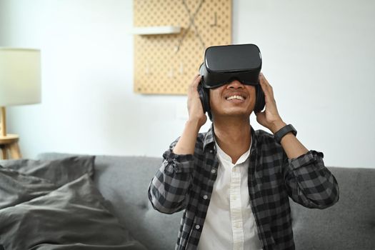 Young man playing video games with virtual reality headset in living room.