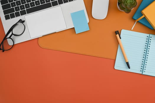 Laptop computer, notebook, sticky note and eyeglasses on orange background.