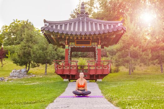 Cheerful young beautiful woman practicing and posing yoga in the east Asian park.