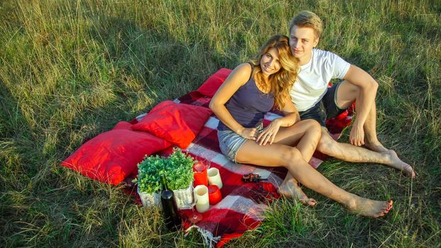 Beautiful young happy loving couple on picnic lying down on plaid on sunny summer day enjoying and resting. looking at camera and smiling.