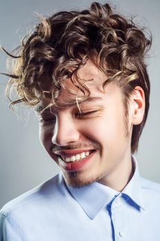 Portrait of young man with curly hairstyle. studio shot. toothy smile and closed eyes.