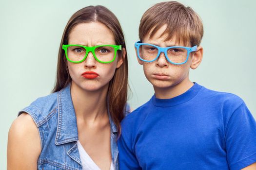 Family, bad emotions and feelings. Older sister and her brother with freckles, posing over light blue background together, looking at camera with unhappy faces. Studio shot