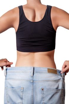 Close-up of slim waist of young woman in big jeans showing successful weight loss, isolated on white background, diet concept.