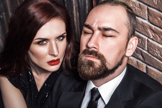 Passion concept, closeup. Bearded man closed eyes, redhead sensual woman with red lips and handsome makeup, looking at camera. Studio shot