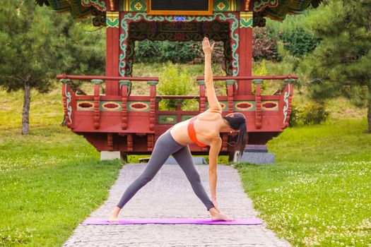 Cheerful young beautiful woman practicing and posing yoga in the east Asian park.