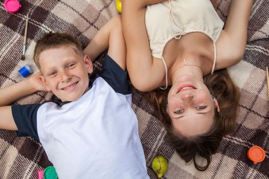Happy young beautiful sister and brother with freckles on their faces posing lying down on plaid and smiling and looking at camera with toothy smile.