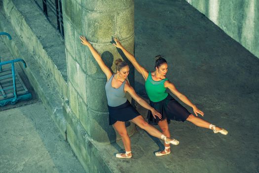 Two young beautiful twin sister dancing ballet in the city with ballet costume. urban sync dance. industrial street dancing. with special effect. synced posing. pointe ballet shoes and dress.