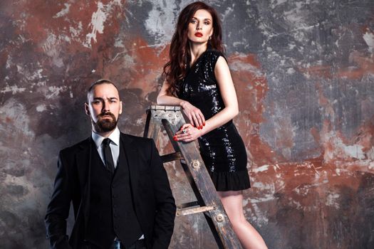 Closeup bearded businessman and ginger woman standing on old stepladder. Studio shot, isolated on vintage, old wall.