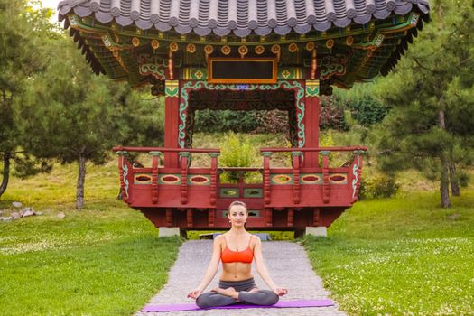 Cheerful young beautiful woman practicing and posing yoga in the east Asian park. baddha konasana pose.