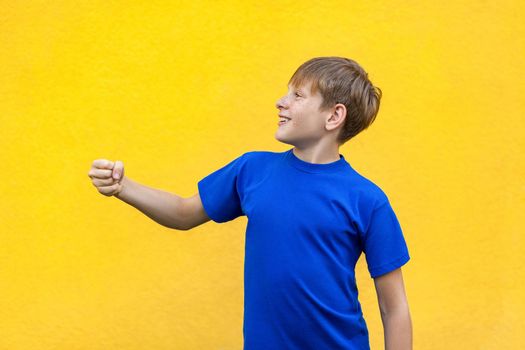 Funny freckled boy holding imaginary object. Studio shot, isolated on yellow background