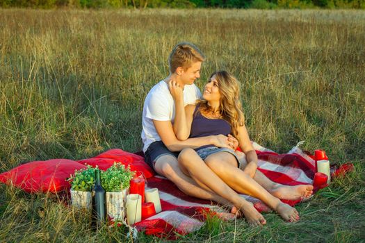 Beautiful young happy loving couple on picnic lying down on plaid on sunny summer day enjoying and resting. hugging and looking at each other and smiling.