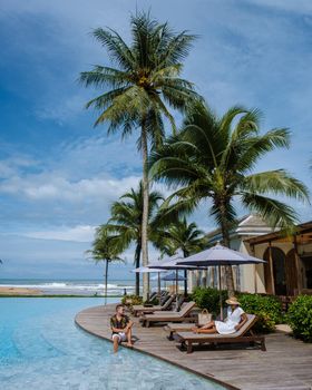 a young couple of men and women at a swimming pool during a vacation on a tropical island. man and woman in infinity pool during sunset. luxury vacation in Thailand pool of a luxury pool villa