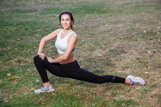 Young happy beautiful sexy girl is stretching in the park garden. people background. with dark hair and black and white sport suit and happiness and smile. on summer or autumn time season.