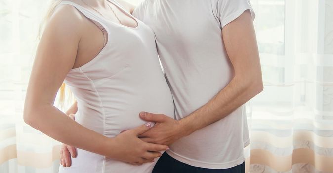 A pregnant woman and a father of a child hug a belly. Selective focus. NATURE.