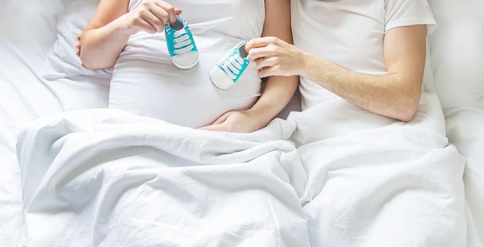 Pregnant woman and man hug belly and hold baby shoes. Selective focus. People.