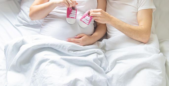 Pregnant woman and man hug belly and hold baby shoes. Selective focus. People.