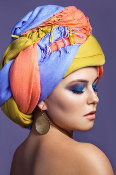 Beautiful woman with colored headwear and blue makeup, studio shot on purple background