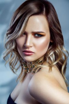 Beauty portrait of beautiful fashion model with makeup, colored wavy hairstyle and accessories on her neck. studio shot on blue background. .