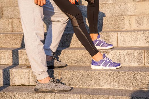 running couple resting. Closeup of running shoes and girl standing with boyfriend during jogging workout training outdoors on steps to relaxing..