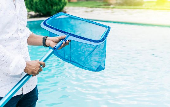 Hands holding a skimmer with blue pool in the background. A man cleaning pool with leaf skimmer. Man cleaning the pool with the Skimmer, Person with skimmer cleaning pool