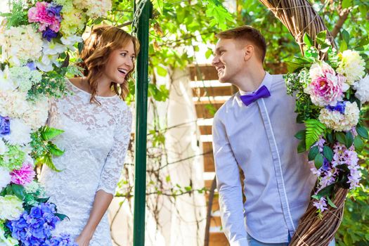 Couple posing in an arch of flowers, looking each other. Outdoor shot, spring park or summer concept. Love, sensual people