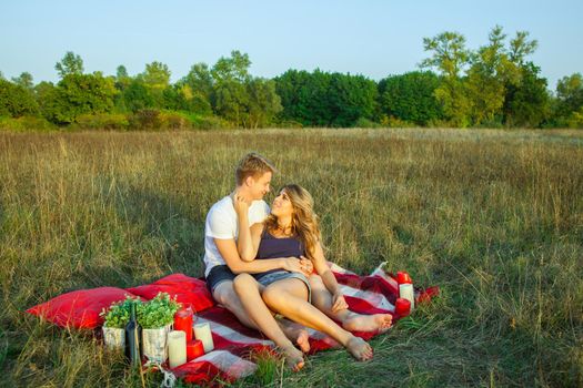 Beautiful young happy loving couple on picnic lying down on plaid on sunny summer day enjoying and resting. hugging and looking at each other and smiling.