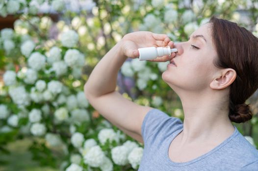 Caucasian woman uses a nasal spray while walking in the park