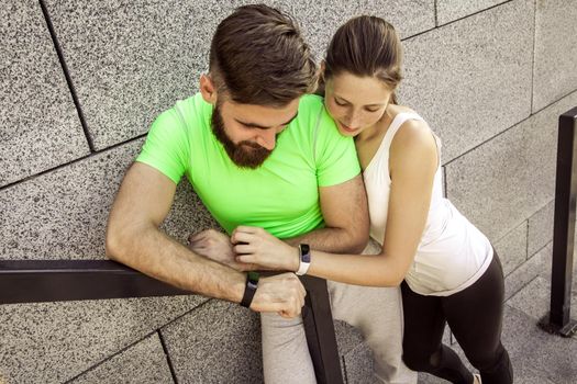 Young sporty couple are resting and check their fitness watch together. sport and technology concepts.