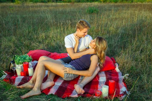 Beautiful young happy loving couple on picnic lying down on plaid on sunny summer day enjoying and resting. hugging and looking at each other and smiling.