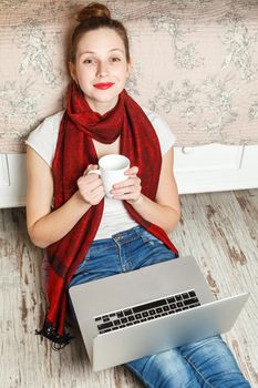 Ecommerce woman. Young female using computer for online shopping, sitting on the floor and drinking coffee.