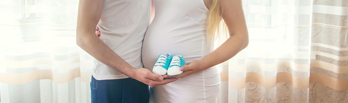 Pregnant woman and man hug belly and hold baby shoes. Selective focus. People.