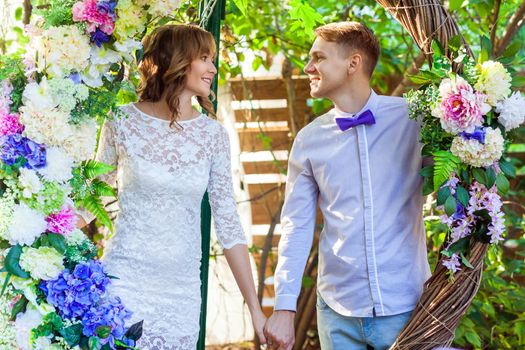 Happiness couple posing in an arch of flowers, holding hands. Outdoor shot, spring park or summer concept. Love, sensual people