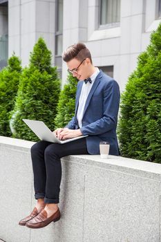 Attractive young businessman with laptop and coffee in hands on office building background. working with laptop and and smilling.