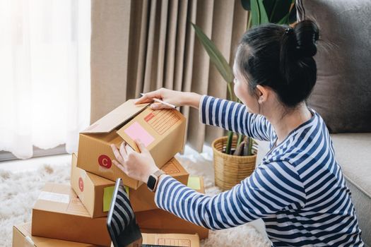 Online merchandising business idea, a beautiful girl is packing the products in the parcel delivery box to prepare the delivery to the customer according to the order received from the customer