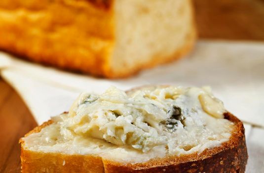 Gorgonzola cheese spread on slice of bread , in the background a loaf of bread , ready to eat