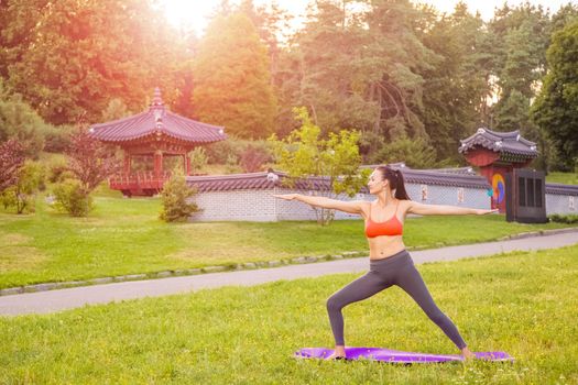 Cheerful young beautiful woman practicing and posing yoga in the east Asian park.