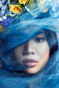 portrait of sensual asian beautiful woman with floral hat and blue veil on light grey background, closeup . indoor studio shot.