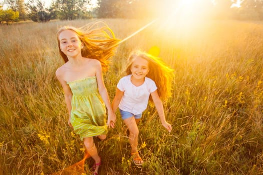 two sisters enjoying together at summertime. jumping and running in the park on sunset and happy