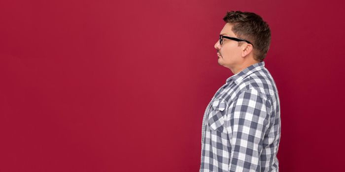 Profile side view portrait of serious handsome middle aged business man in casual checkered shirt and eyeglasses standing and looking forward. indoor studio shot, isolated on dark red background.