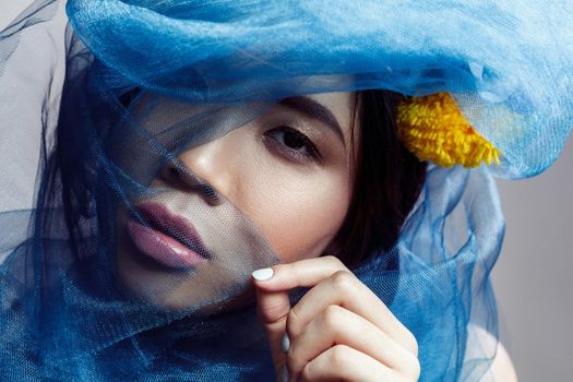 portrait of sensual gorgeous asian woman looking at camera through blue veil on face . indoor studio shot.