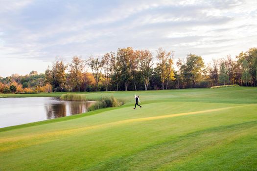 Autumn, lake, golf course. Young adult girl running on the green grass of the golf course. The girl freedom. Outdoor