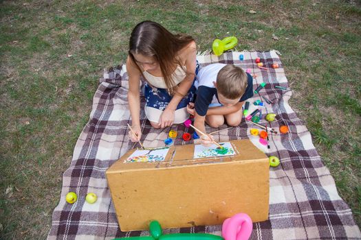 Older sister trying to teach her brother to paint and posing in the park on summer time, drawing and painting.