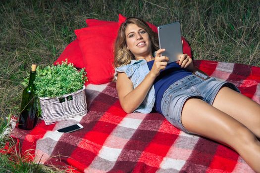 Portrait of woman lie down and holding tablet on summertime outdoor