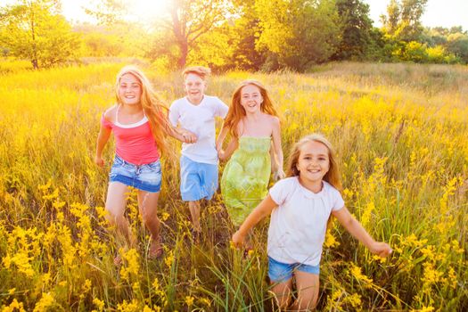 four happy beautiful children running playing moving together in the beautiful summer day. jumping and looking at camera with happiness and toothy smile.